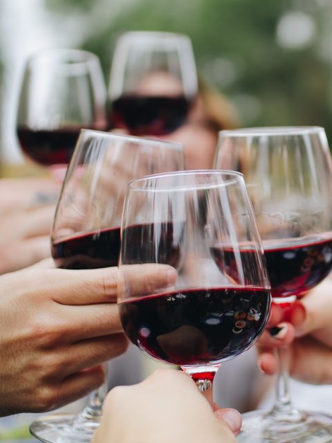 Mehrere Gäste stoßen im Außenbereich mit Gläsern Rotwein an.
