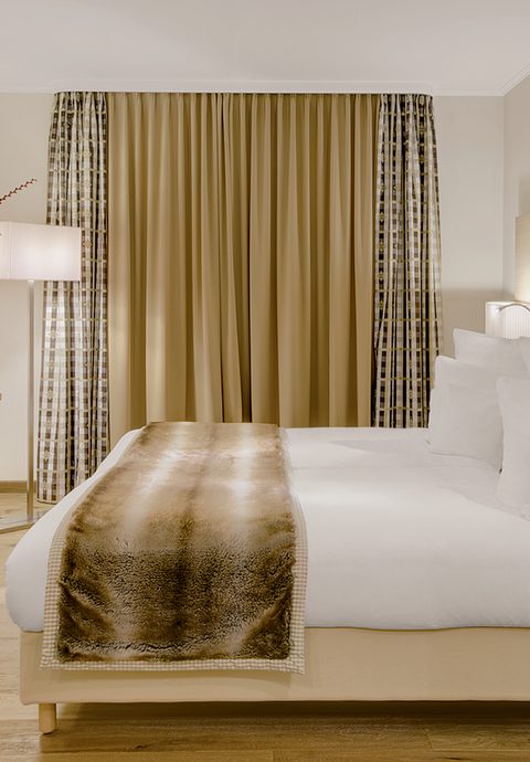 Modernes Hotelzimmer mit Doppelbett, Kissen, Kommode, Fernseher und geschlossenen Vorhängen.