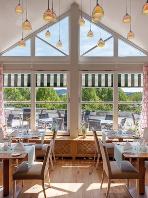 Heller Restaurantbereich mit gedeckten Tischen, großer Fensterfront und Blick auf die Terrasse.