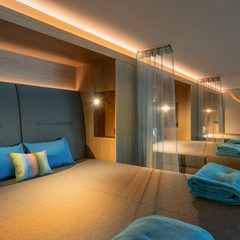 Moderner Wellness-Ruheraum mit mehreren gepolsterten Liegen, Kissen, Handtüchern und indirekter Beleuchtung.