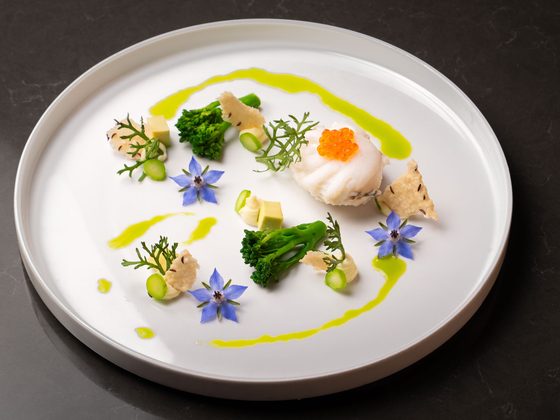 Kreativ angerichtetes Fischgericht mit grünem Gemüse, Kaviar und essbaren Blüten auf weißem Teller.